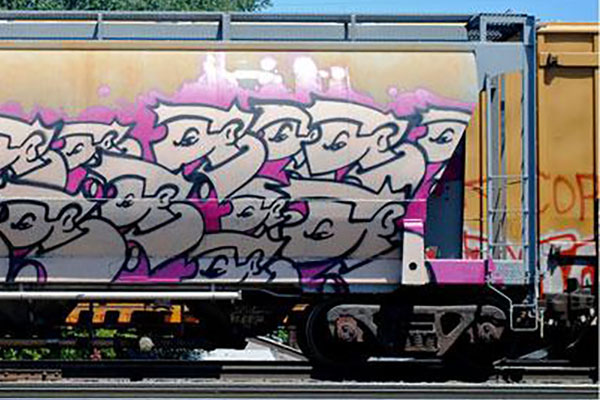 image of train graffiti depicting multiple face profiles on the side of a hopper car